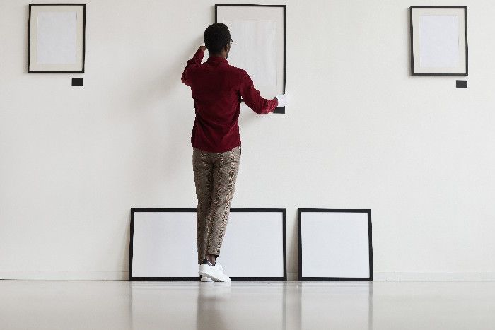 Ein Mann hängt Bilder in einer Galerie auf.